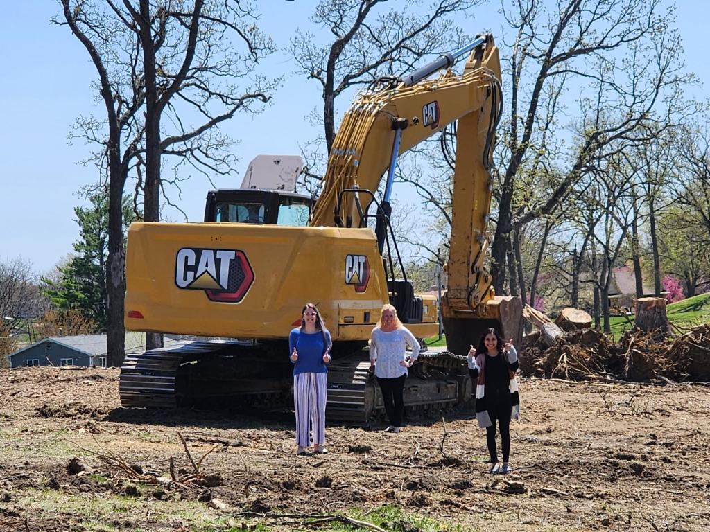 Gwen, Lesa, and Dahiana in front of an excavator